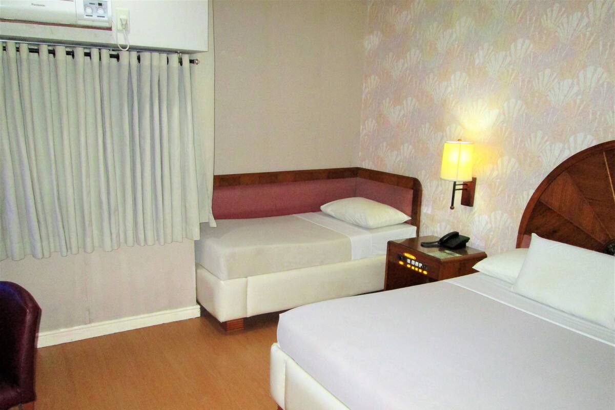 A hotel room with a large bed, a smaller bed, a desk with a lamp, and a chair.