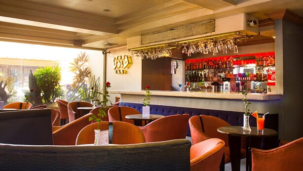 A bar area with orange chairs, a bar counter with bottles, and a decorative wall with a logo. - Grand City Hotel (Cagayan de Oro)