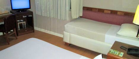 Habitación de hotel con una cama grande, otra más pequeña, un escritorio con una computadora y una mesita de noche con lámpara.