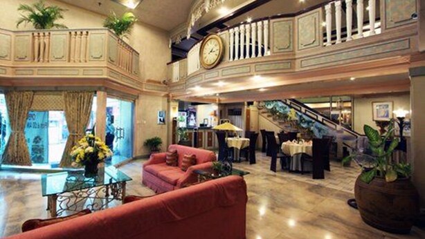 A spacious lobby with a staircase, a clock, and a seating area with a sofa and tables. - Manila Manor Hotel (Manila)