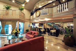 A spacious lobby with a staircase, a clock, and a seating area with a sofa and tables. - Manila Manor Hotel (Manila)