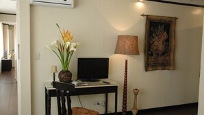 A room with a desk, a television, a lamp, a vase with flowers, and a painting on the wall. - Manila Manor Hotel (Manila)