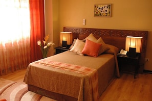 A neatly made bed with a patterned bedspread, two bedside lamps, and a vase of flowers on the nightstand. - Manila Manor Hotel (Manila)