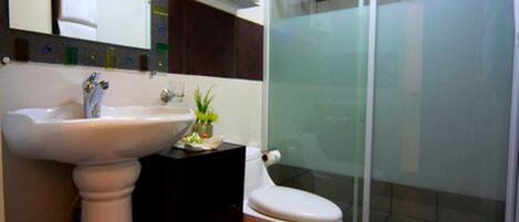 Un baño con lavamanos pedestal, inodoro y cabina de ducha de vidrio.