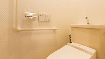 A small, clean bathroom with a toilet, a shelf with a toilet paper holder, and a wall-mounted control panel.