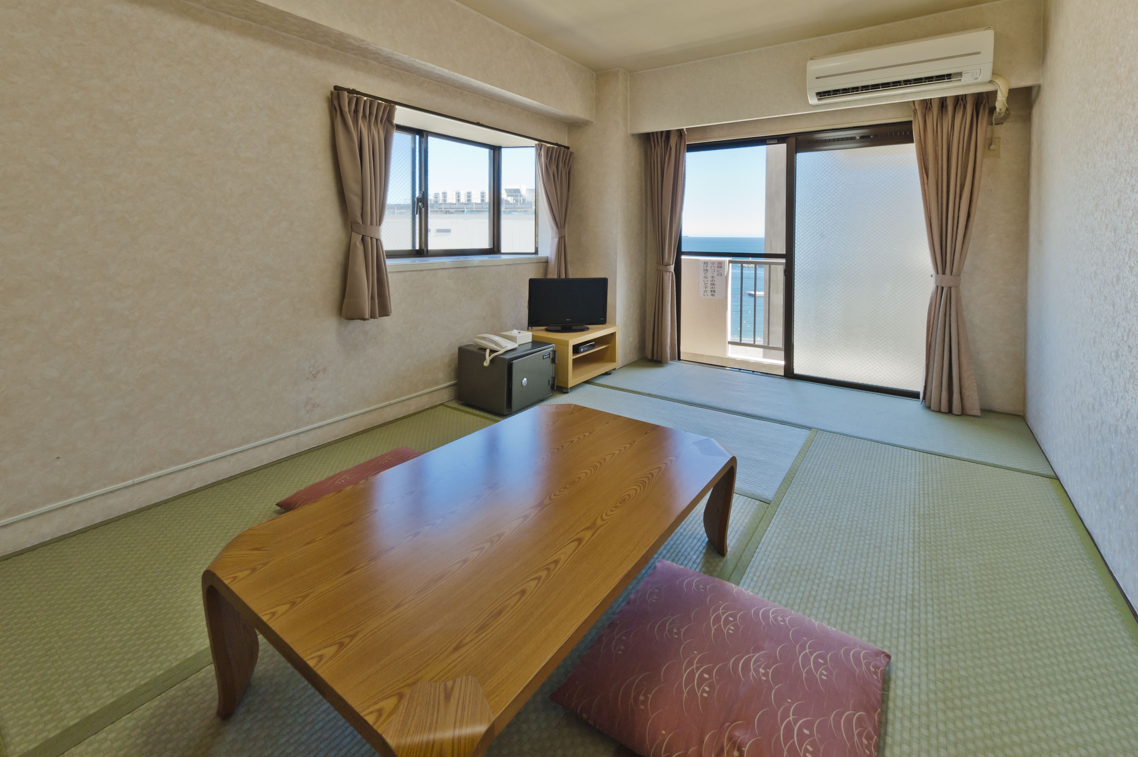 A room with tatami mat flooring, a wooden table, a television, and a sliding door leading to a balcony.