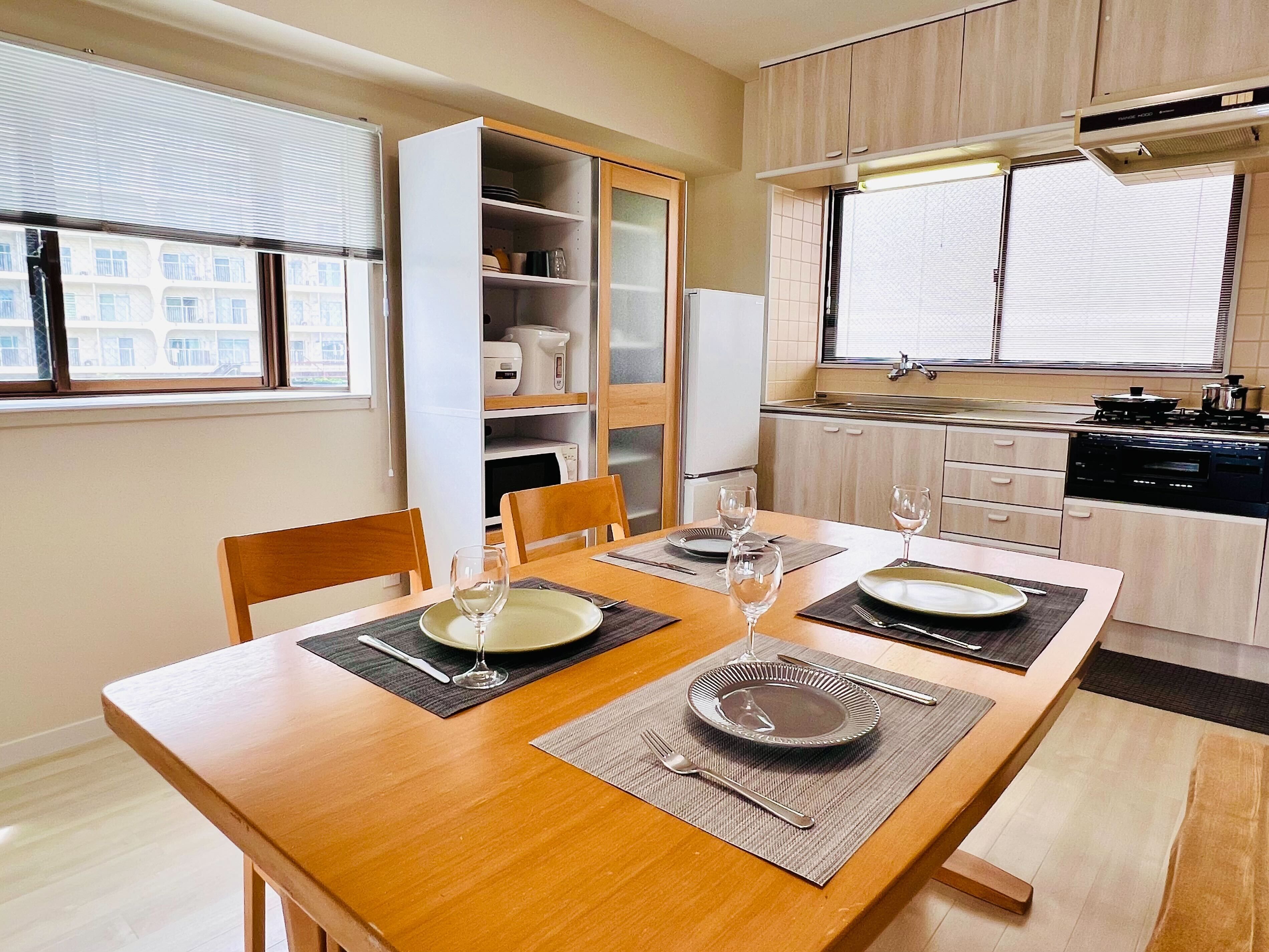 A dining area with a wooden table set for two, a kitchen with modern appliances, and a view of the city through the window.