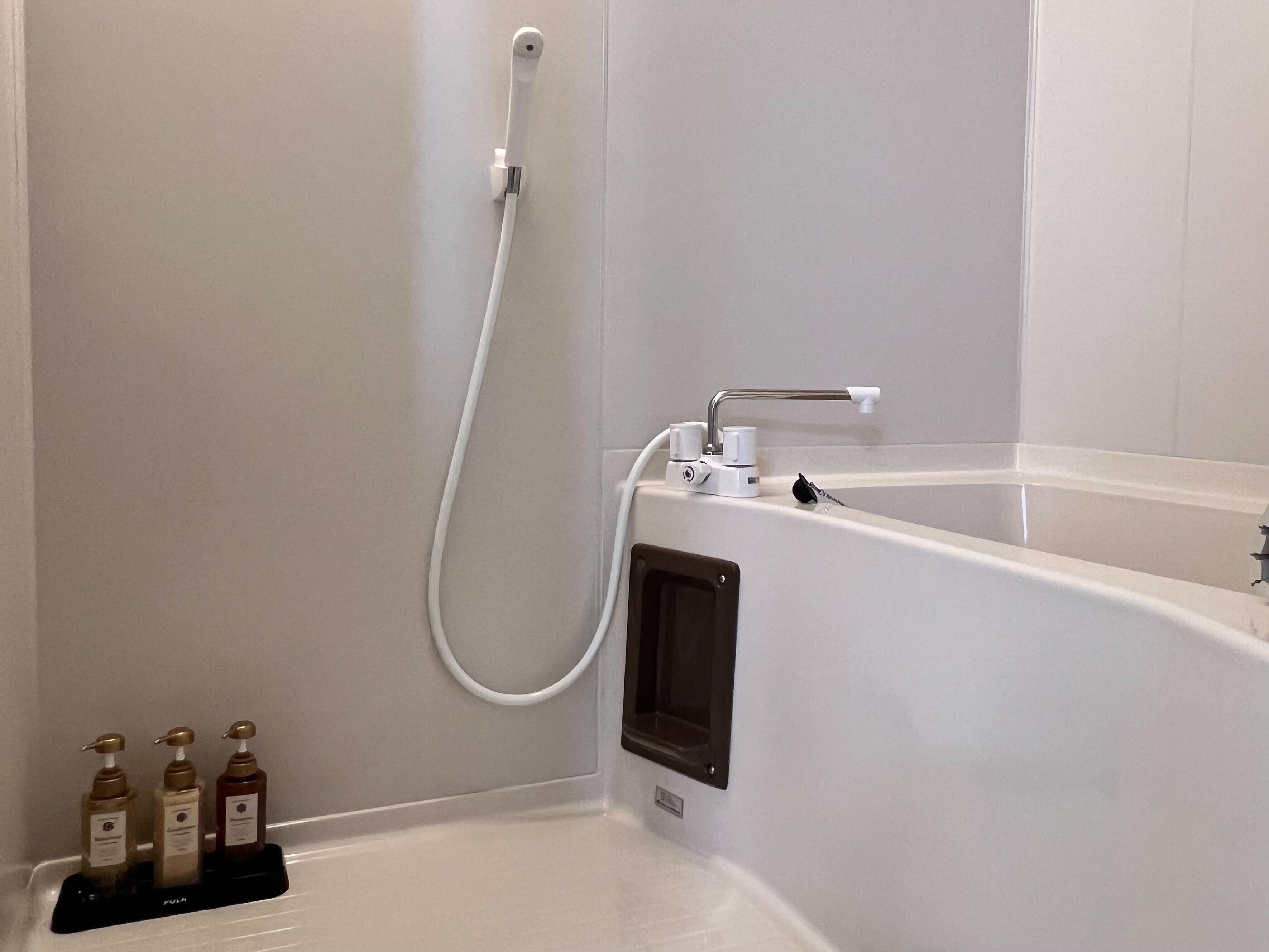A bathroom with a bathtub, a shower, and three bottles of toiletries on a tray.