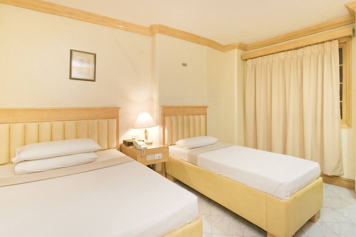 Ein Hotelzimmer mit zwei Betten, einem Nachttisch mit Lampe und einem Fenster mit Vorhängen.