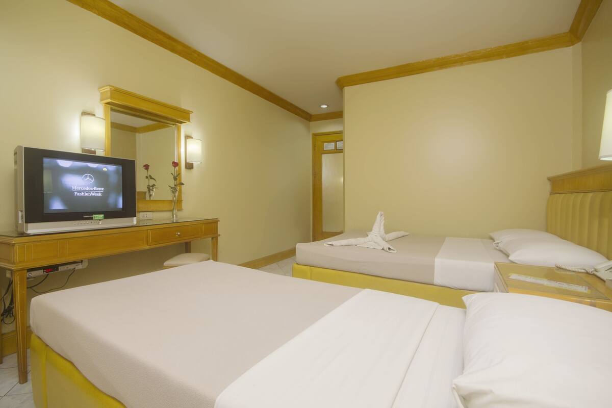 Ein Hotelzimmer mit zwei Betten, einem Fernseher auf einem Schreibtisch und einem Spiegel.