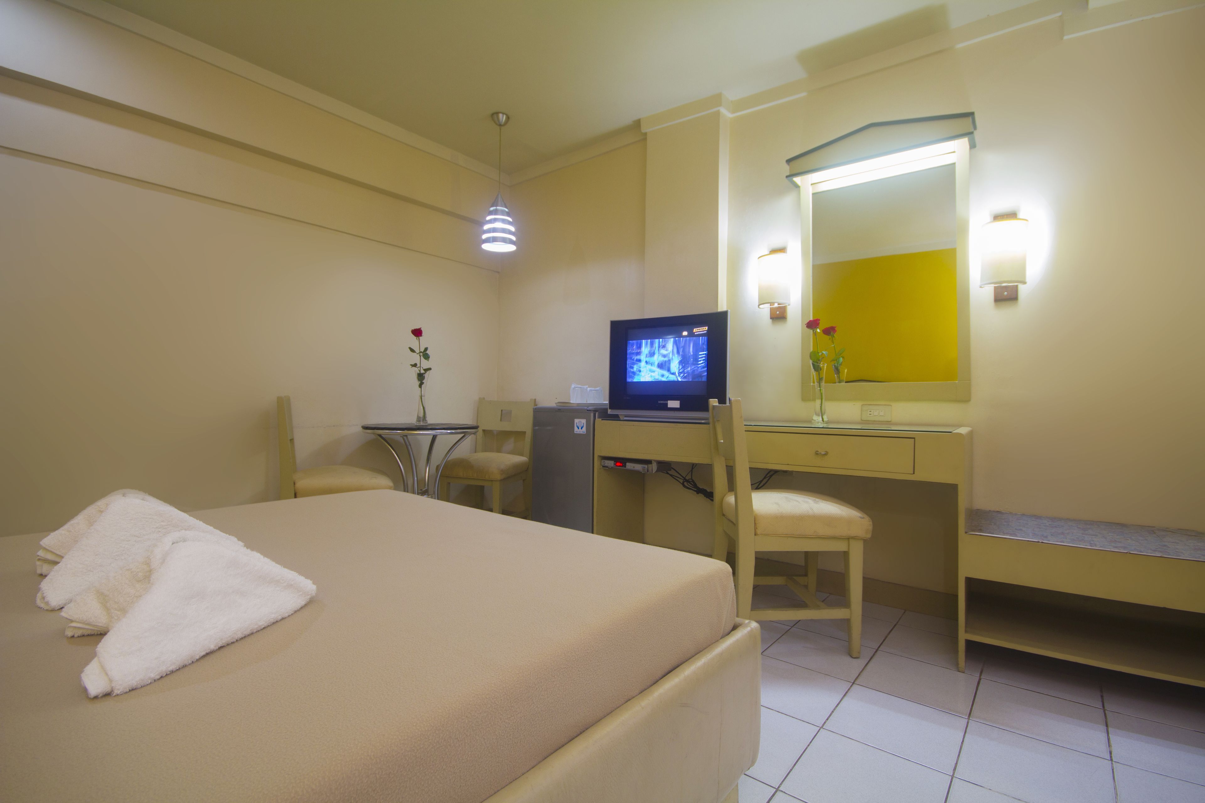 Una habitación de hotel con cama, escritorio, silla, televisor y espejo.