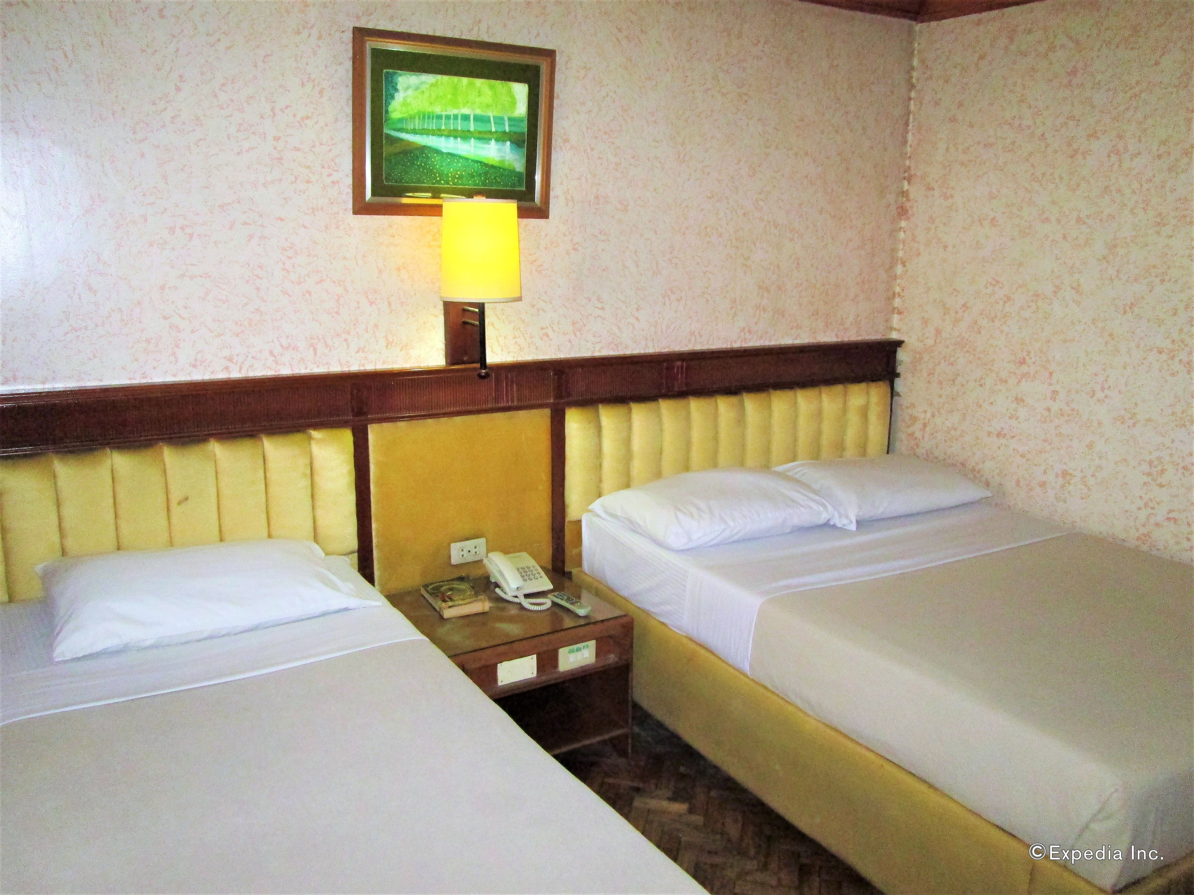 A hotel room with two single beds, a bedside table with a telephone, and a framed picture on the wall.