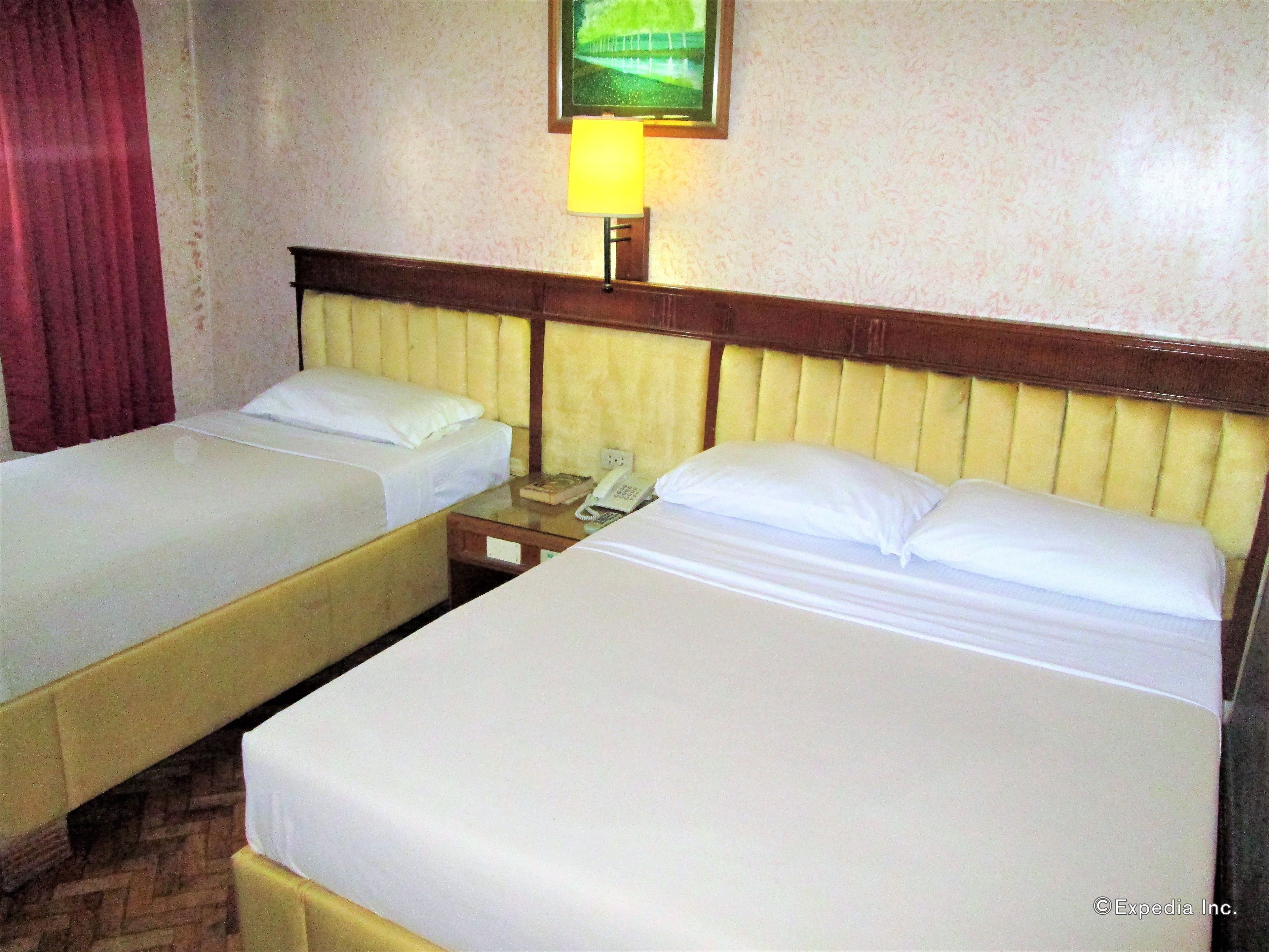 Una habitación de hotel con dos camas individuales, una mesita de noche con lámpara y un teléfono.