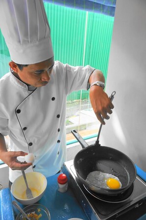 Un cocinero con uniforme blanco cocina un huevo en una sartén sobre una hornilla.