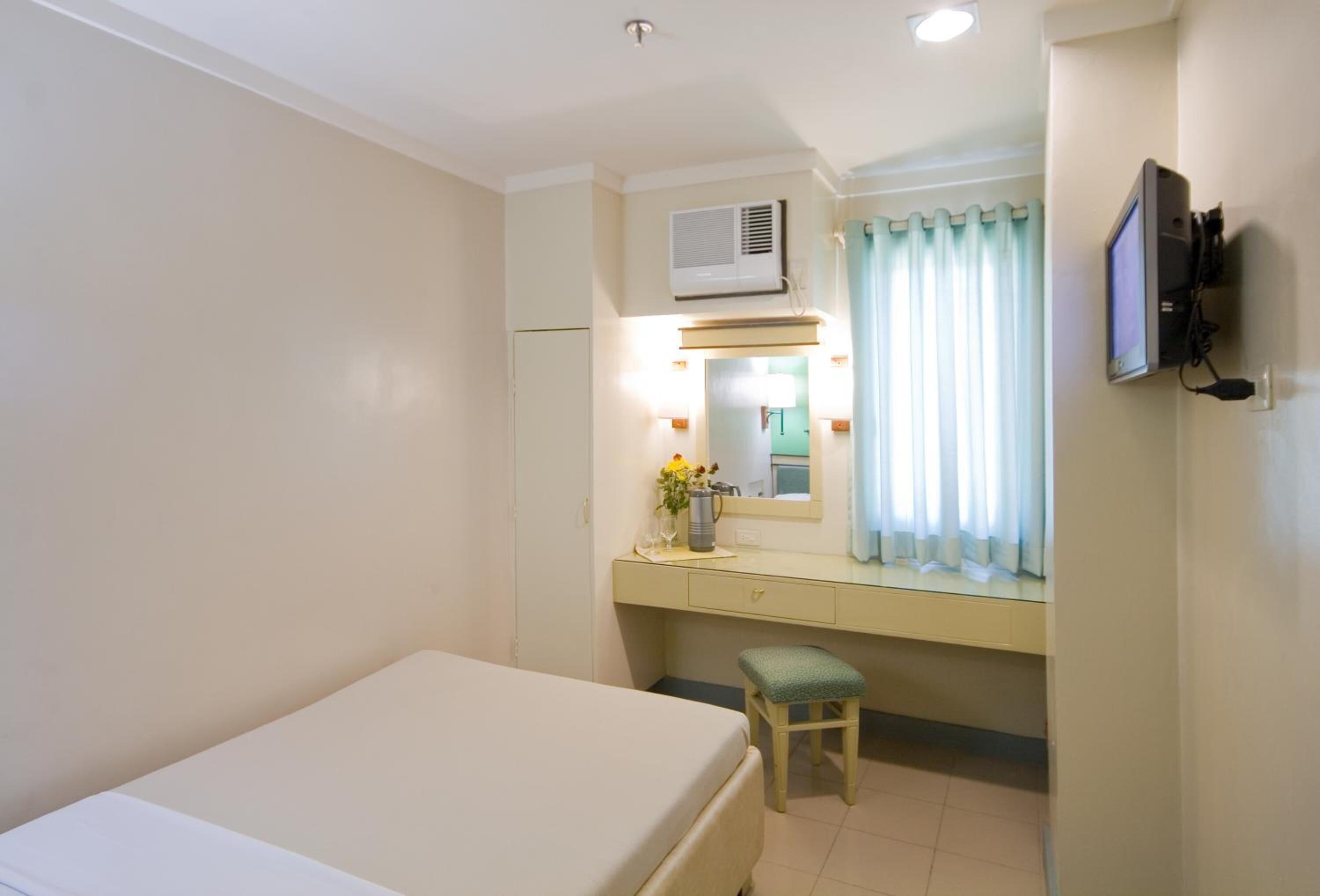Habitación de hotel con cama, escritorio con espejo, televisión y equipo de aire acondicionado.