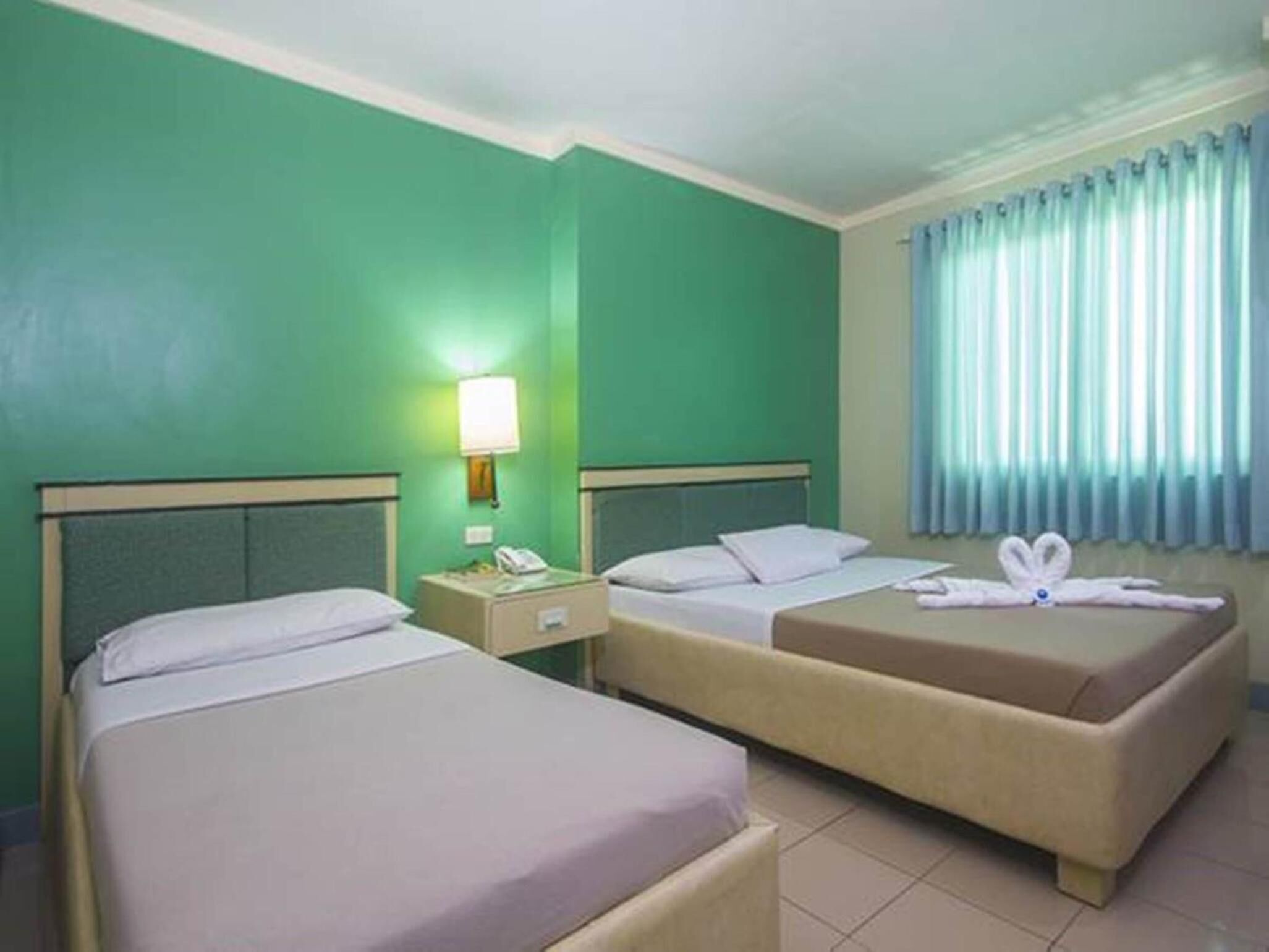 Habitación de hotel con dos camas, una mesita de noche con lámpara y una ventana con cortinas.