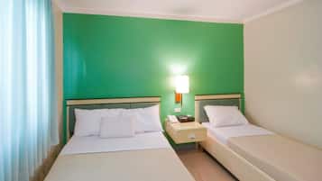 Una habitación de hotel con dos camas, una mesita de noche con lámpara y una pared verde.