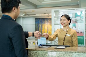A hotel reception area with a receptionist, a man handing over a credit card, and a poster advertising a room. - New Dawn Pensionne (Cagayan de Oro)