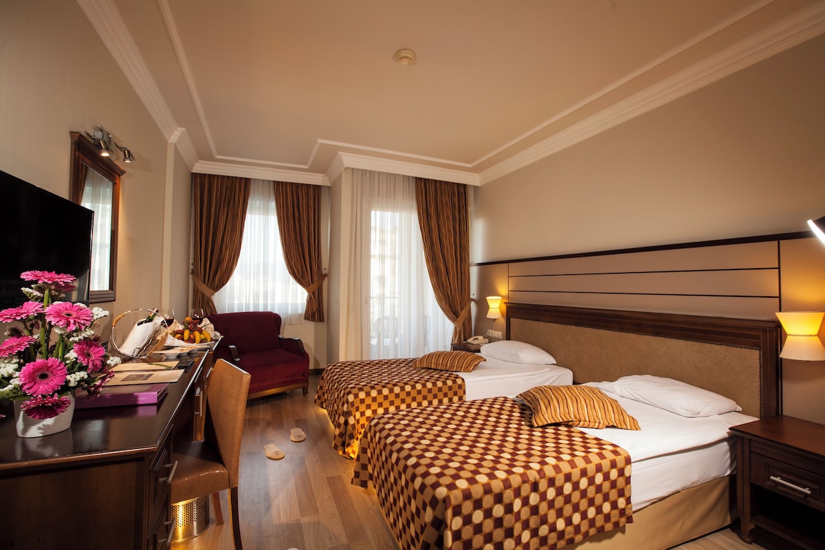 A hotel room with two beds, a desk with a computer, a chair, a TV, and a vase of flowers.