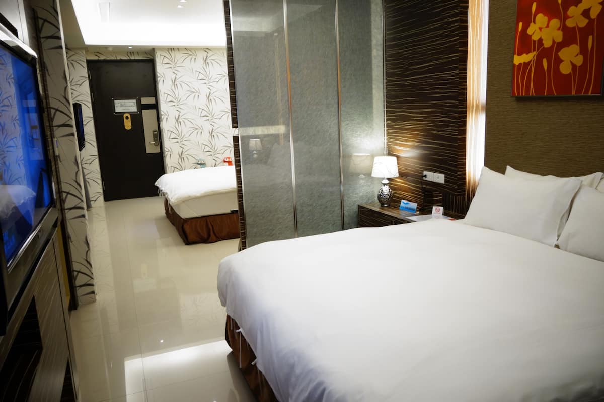 Quarto de hotel com uma cama grande, televisão, escrivaninha com luminária e espelho.