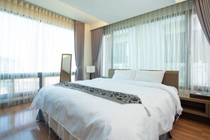 A modern hotel room with a large bed, a bedside table, a mirror, and sheer curtains.