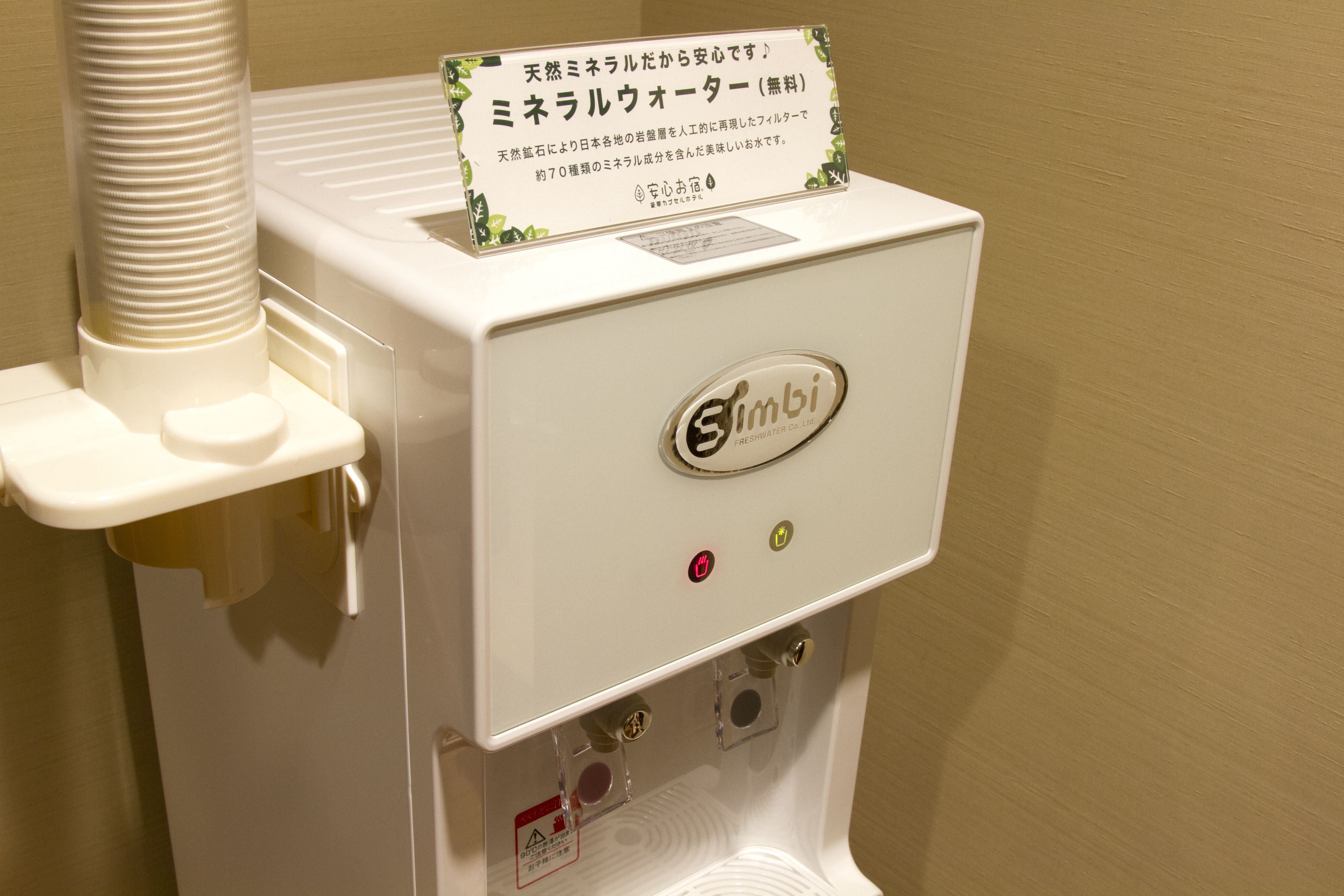 A white water dispenser with a sign in Japanese, a control panel with buttons, and a water bottle holder.