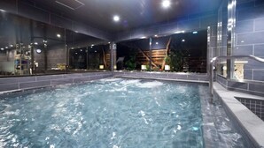 A modern indoor pool area with clear water, surrounded by dark tiles and glass walls.