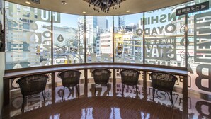A bar area with wicker chairs and a view of the city through large windows.