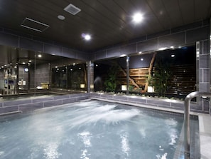 A spa area with a hot tub, glass walls, and a wooden wall with plants. - Anshin Oyado Shinjuku - Caters to Men (Tokyo)