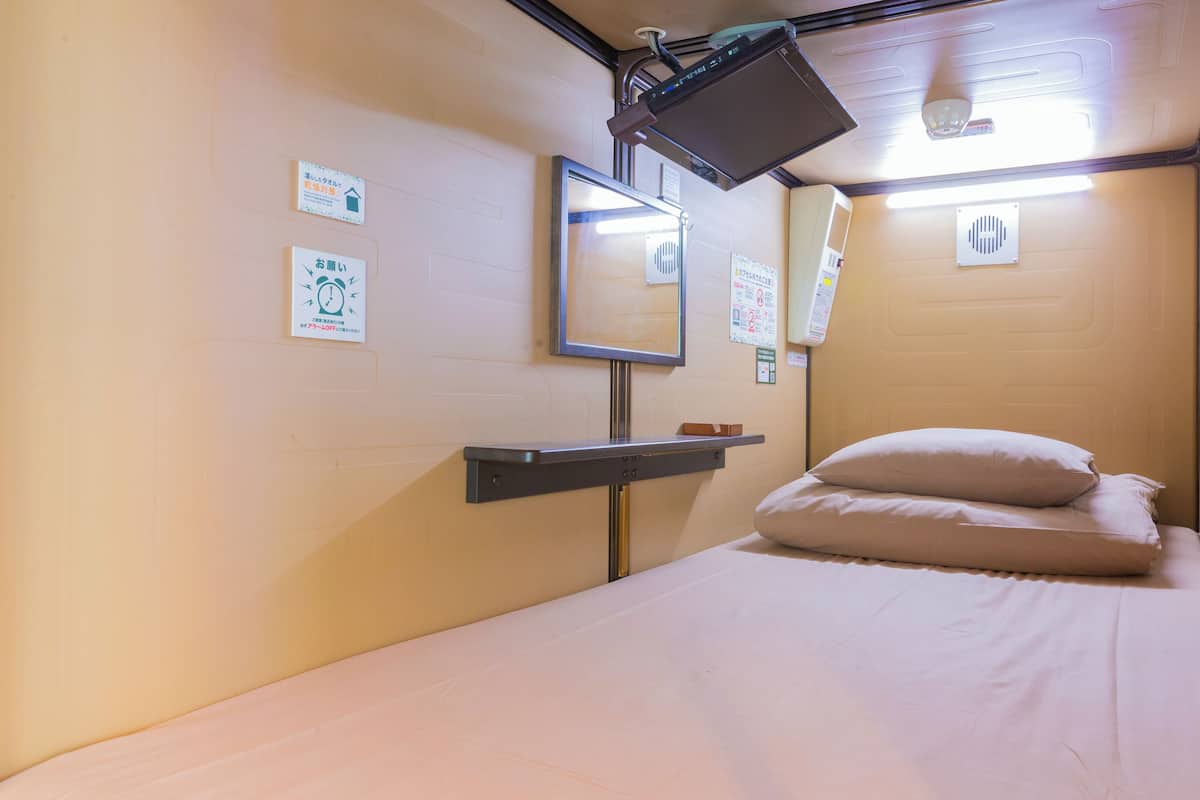 Une petite chambre avec un lit simple, une étagère, un miroir et divers affiches informatives accrochées aux murs.