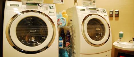 Two front-loading washing machines in a laundry area with a sink and various cleaning products.