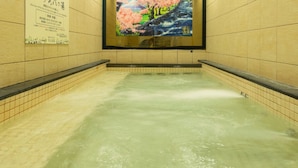 Un baño de aguas termales con paredes de azulejos y un cartel de flores de cerezo.