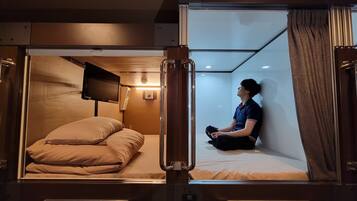 Une chambre compacte et moderne, dotée d’un lit simple, d’un téléviseur fixé au mur et d’une petite table de chevet.