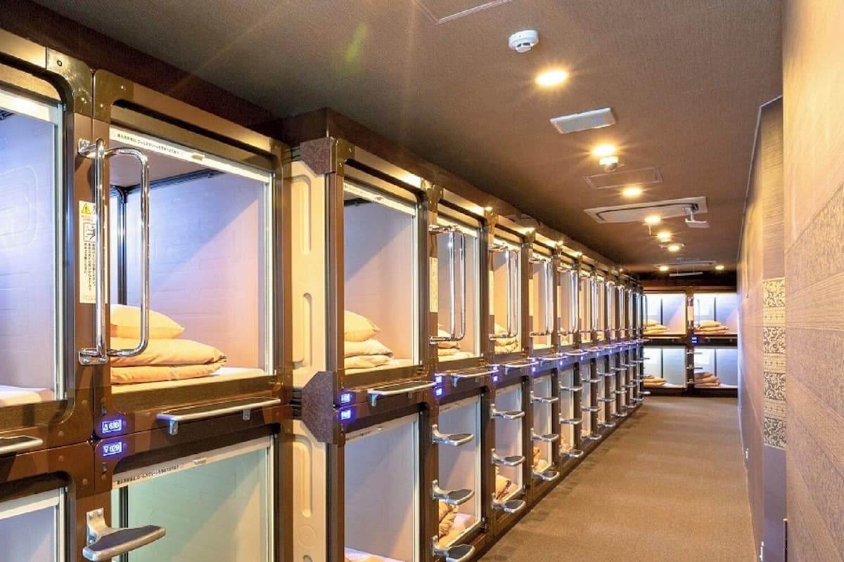 Une rangée de lits superposés avec des structures métalliques et des panneaux de verre, chacun étant équipé d’un petit panneau de commande et d’un oreiller.