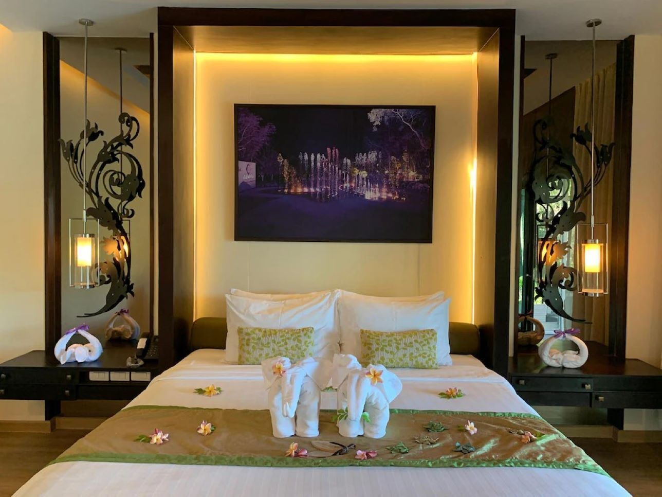 Une chambre d’hôtel avec un grand lit, deux tables de chevet, un tableau accroché au mur et des appliques murales décoratives.