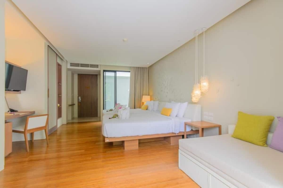 Una habitación de hotel con cama, mesitas de noche, escritorio, televisión y sofá.
