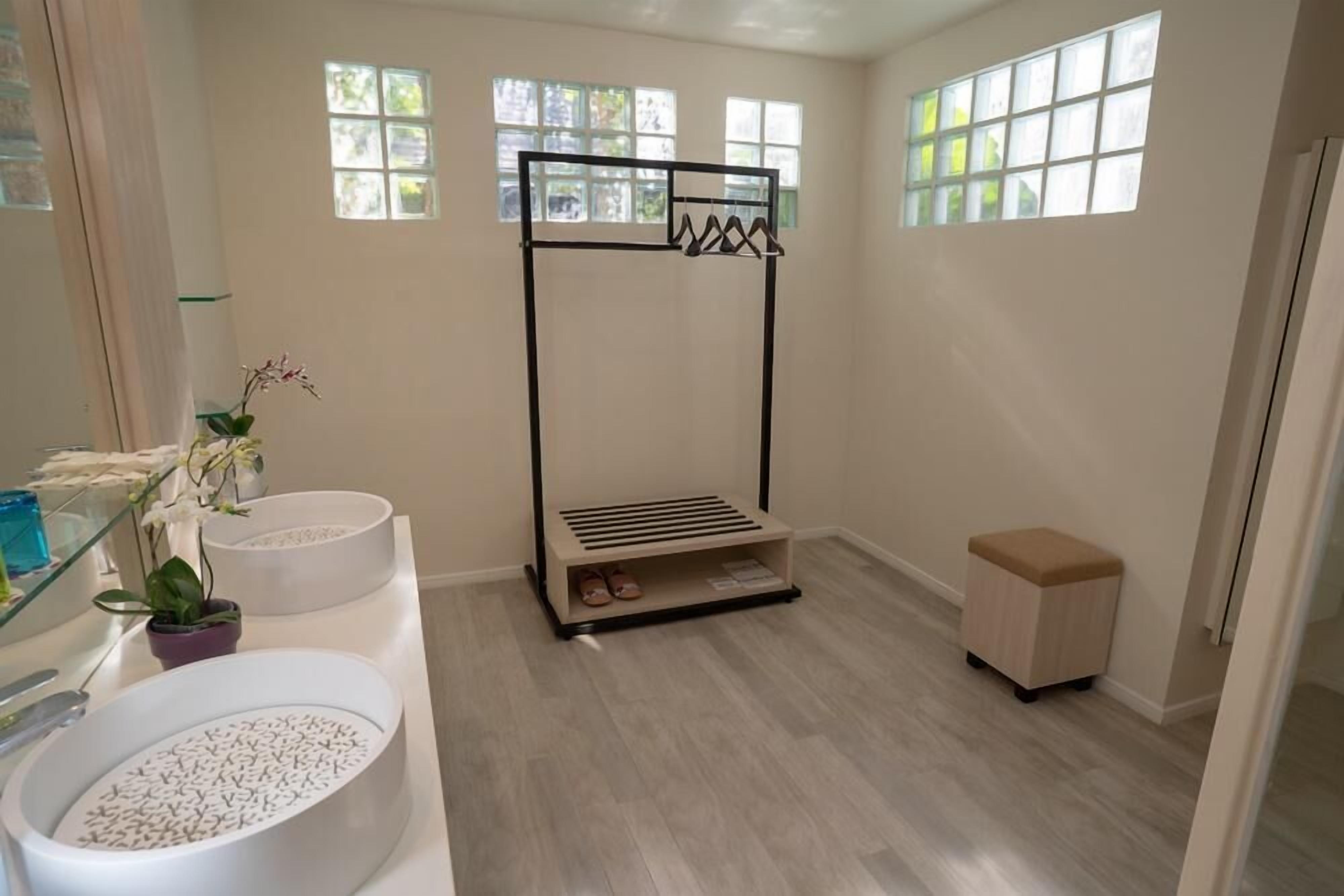 A bathroom with a large white sink, a glass shower enclosure, a black towel rack, and a small wooden stool.