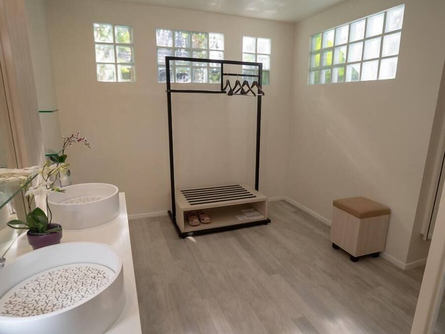 A bathroom with a large white sink, a glass shower enclosure, a black towel rack, and a small wooden stool.