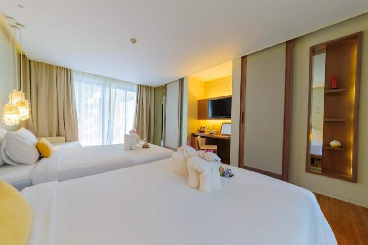 Habitación de hotel con dos camas, televisor, escritorio y espejo.