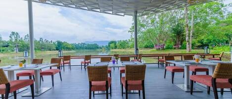 An outdoor dining area with tables and chairs, a view of a lake, and a covered seating area with a view of the surrounding landscape.