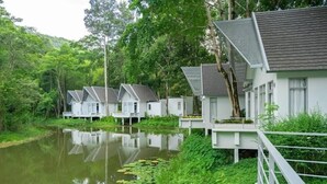 Una hilera de edificios blancos con techos grises, unidos por puentes sobre una masa de agua tranquila, rodeados de abundante vegetación.