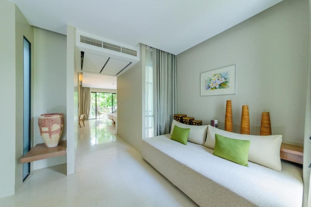 A modern hotel room with a large sofa, a decorative vase, and a painting on the wall.