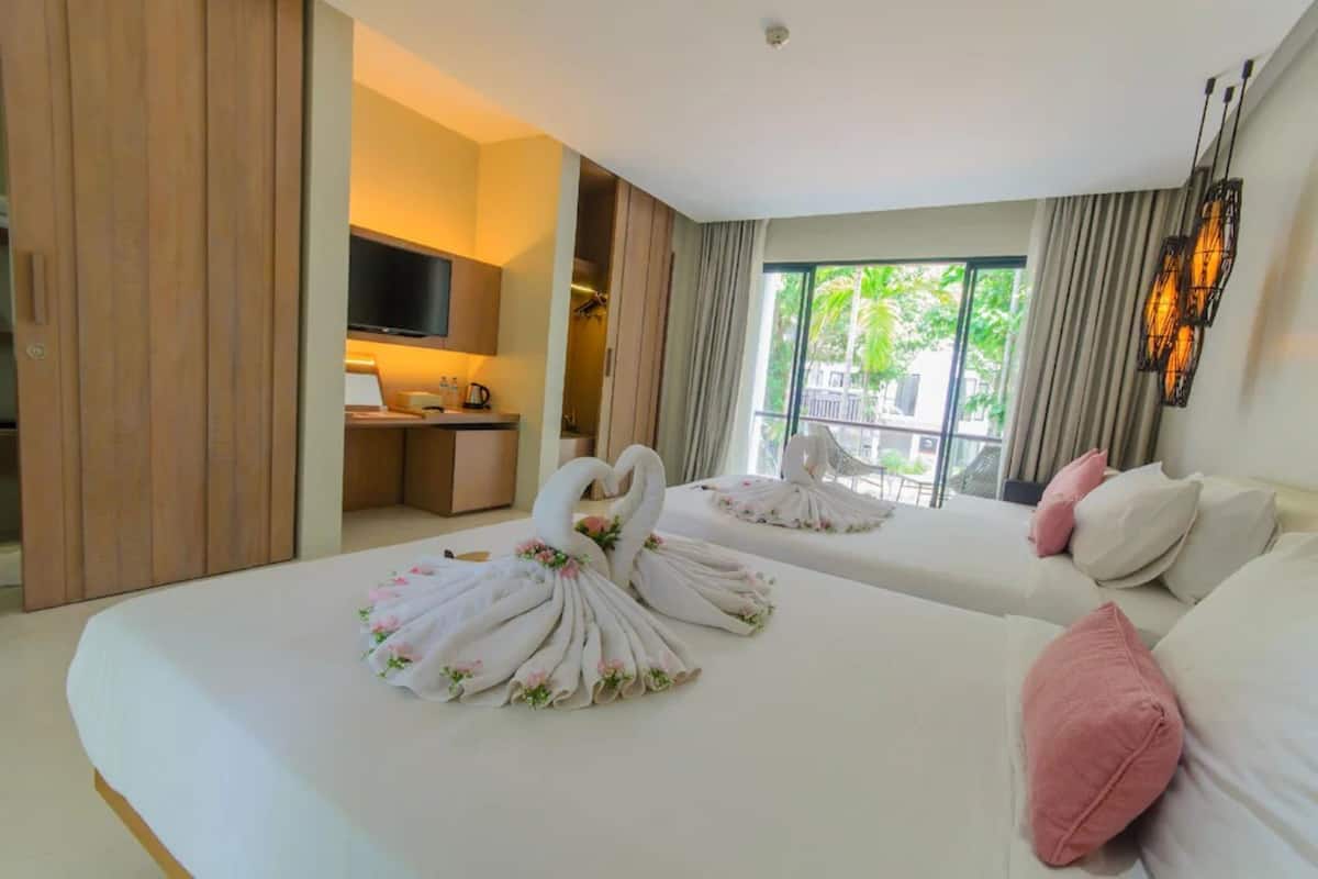 Habitación de hotel con dos camas, televisión, una kitchenette pequeña y un balcón con cortinas.