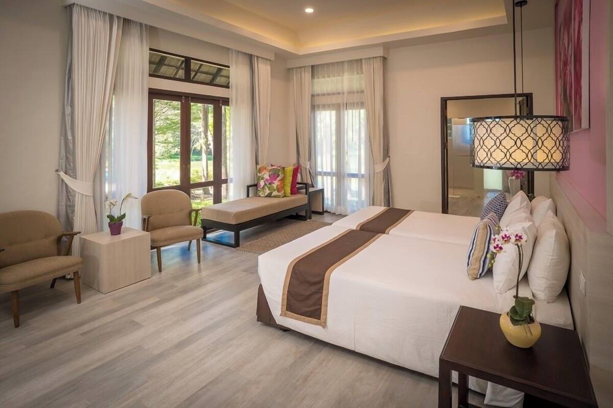 Una habitación de hotel con una cama grande, dos sillones, una mesita y un banco.