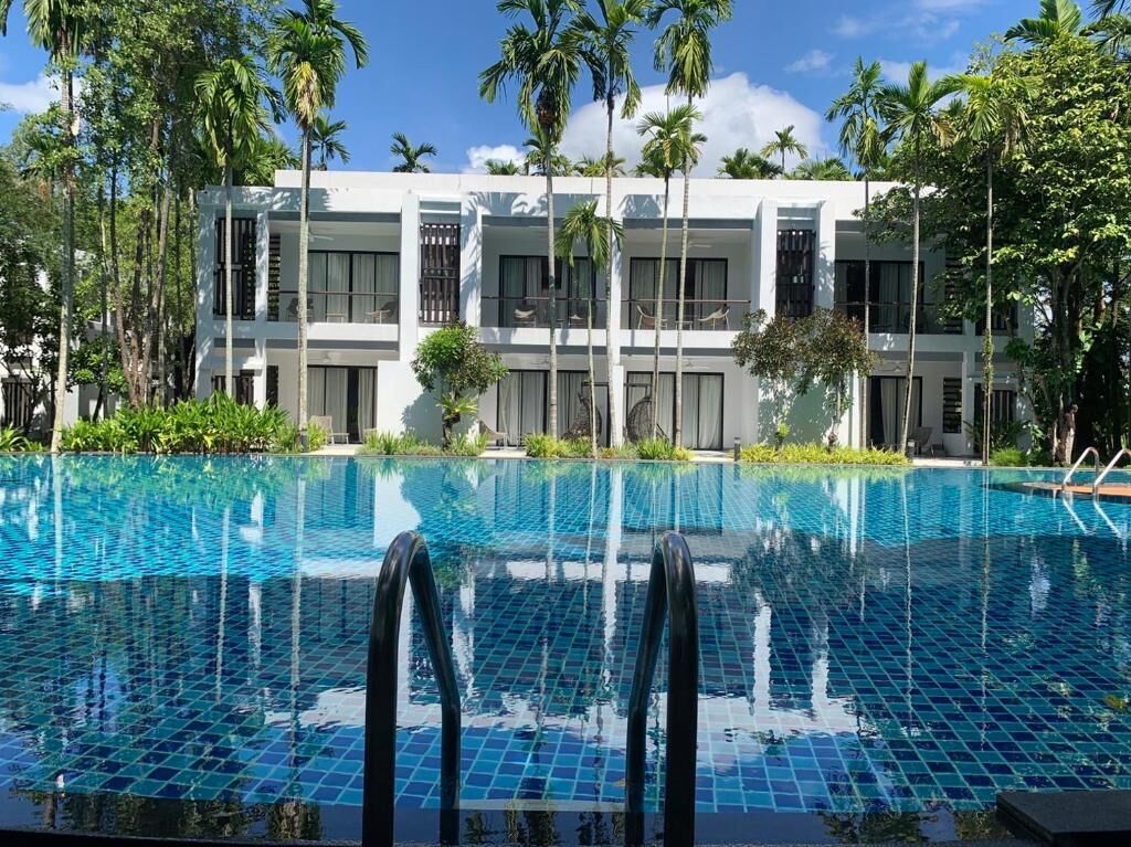 A modern hotel with a pool, surrounded by palm trees and greenery.
