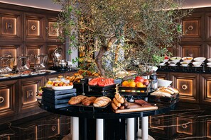 A buffet with various food items, including fruits, bread, and pastries, arranged on a black table with a large tree in the center. - Paris Hotel Yerevan (Yerevan)