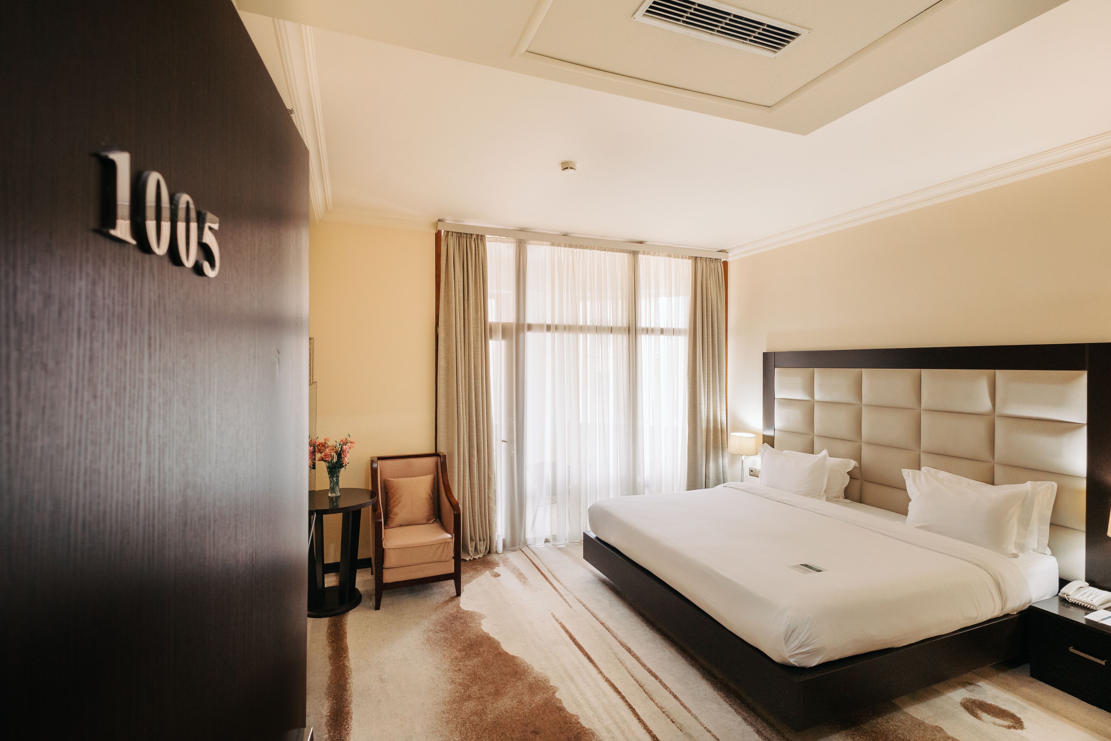 Una habitación de hotel con una cama grande, una mesita de noche, una silla y una ventana con cortinas.
