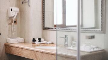 Un baño con encimera de mármol, secador de pelo, espejo y artículos de aseo.
