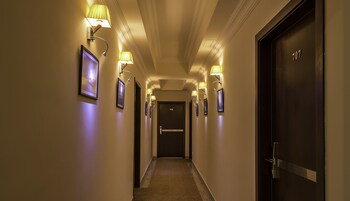 Een hotelgang met ingelijste foto's aan de wanden, een tapijtvloer en een donkere deur met het nummer 707.