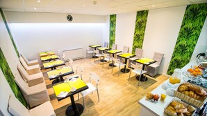 A modern breakfast area with tables, chairs, and a buffet with pastries and fruits. - Hotel Beaulieu (Clermont-Ferrand)